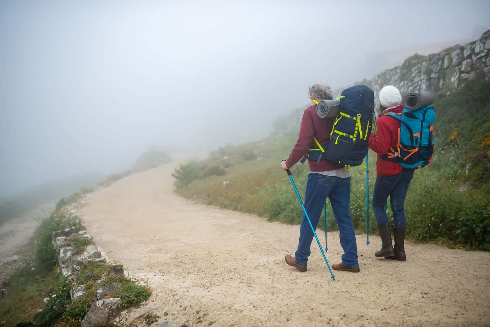 Two hikers with backpacks and poles on a foggy dirt trail