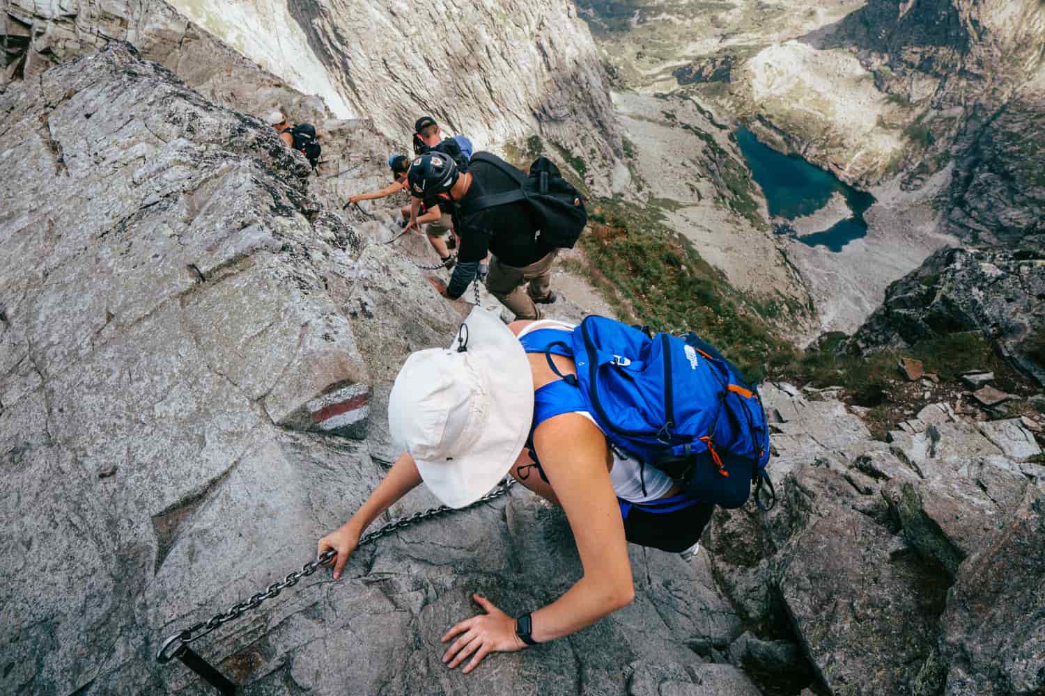 Hikers with backpacks scrambling up a steep rock slab
