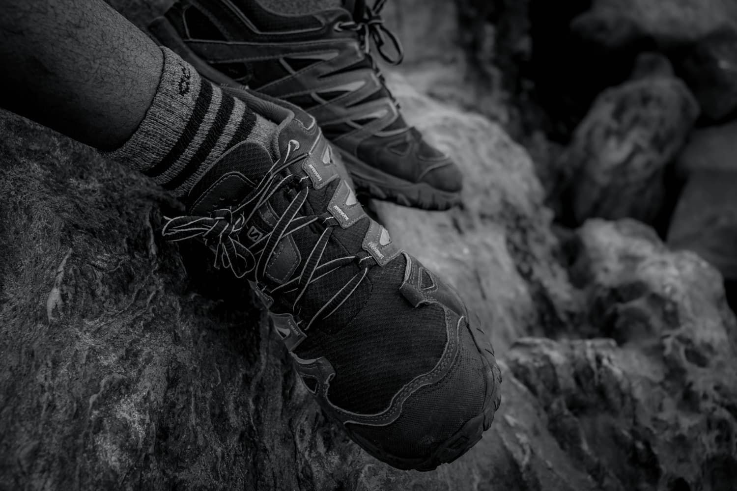 A hiking boot and sock on rock, in black and white
