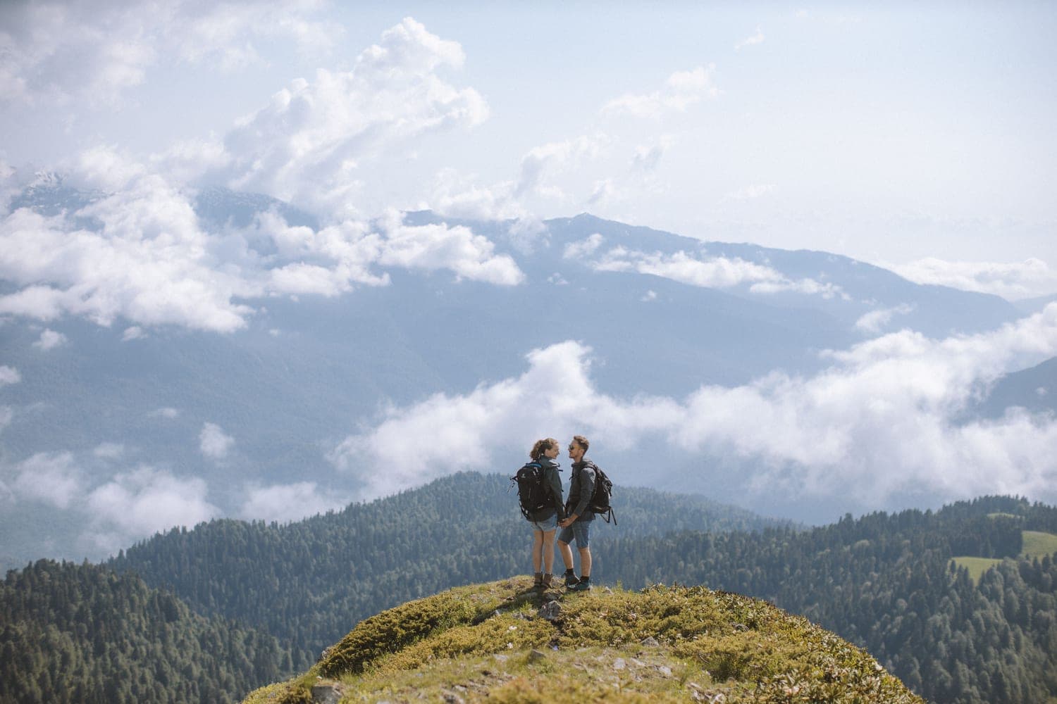 Two hikers standing on a grassy summit above the clouds