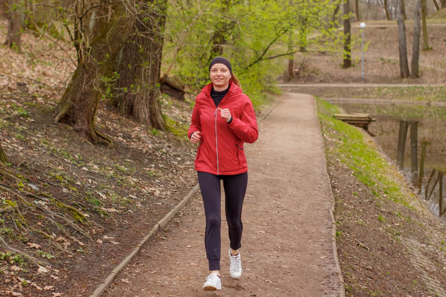 A woman in a red jacket jogging on a forest path