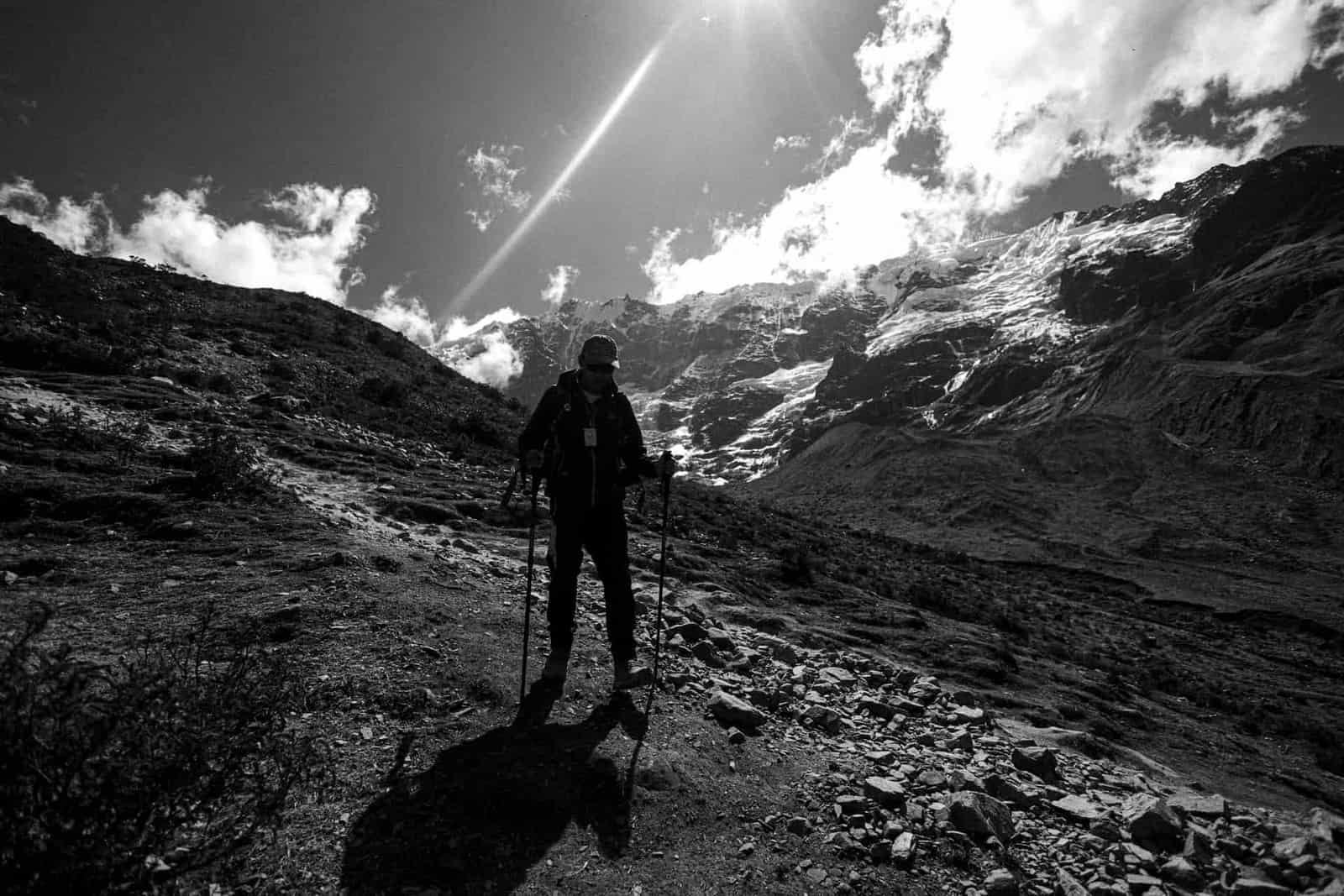 A hiker with poles on a rocky mountain path, in black and white