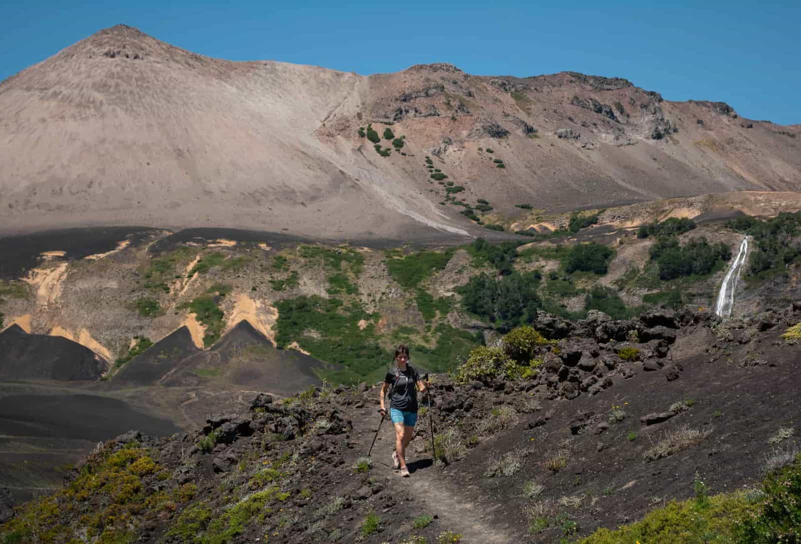 A hiker with trekking poles on a mountain trail under a blue sky