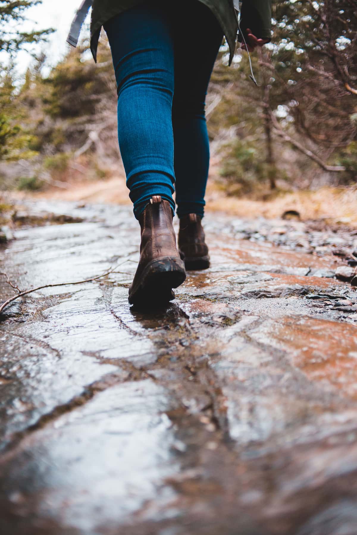 A hiker in jeans and leather boots walking across wet, rough rock