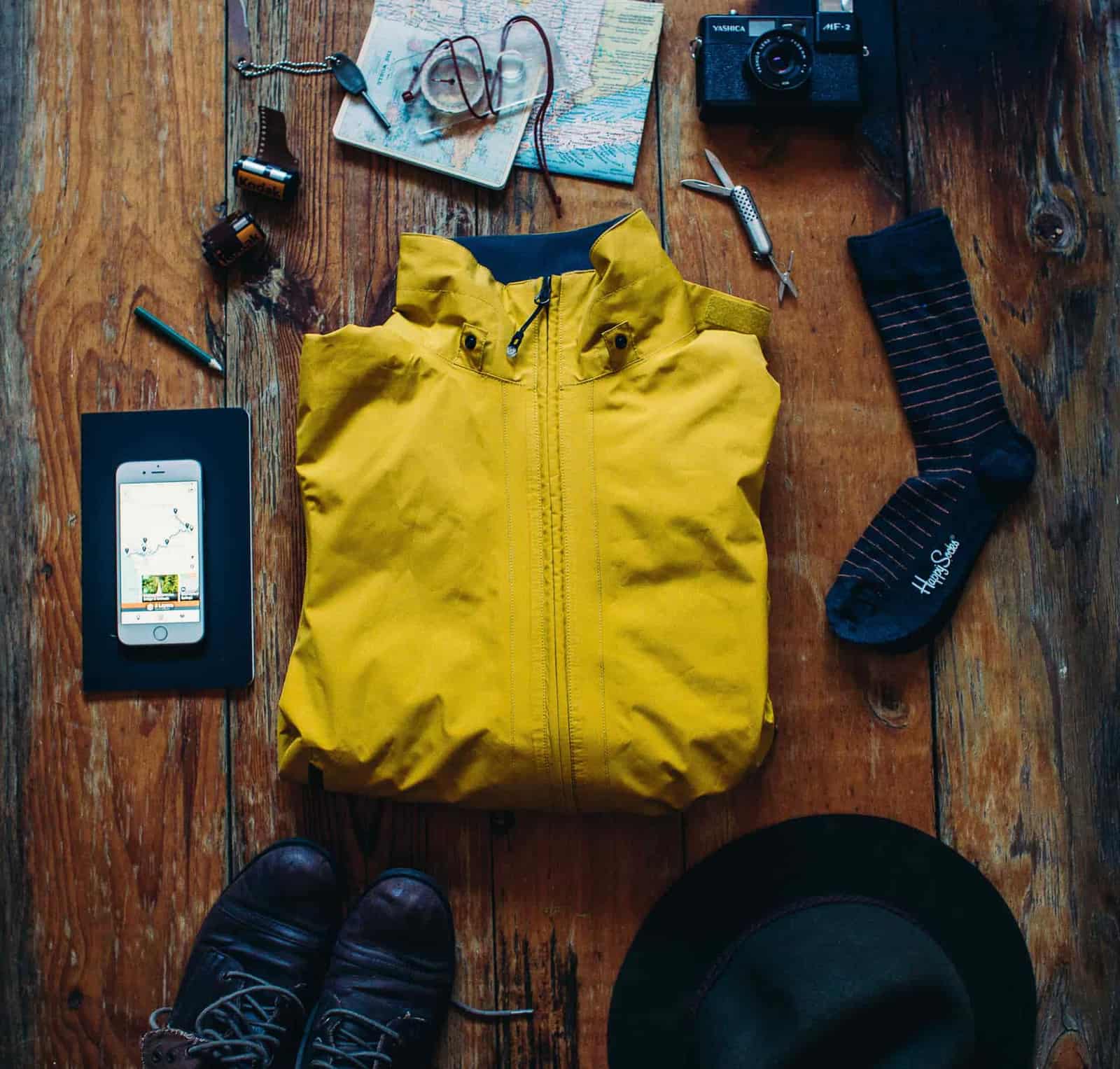 Hiking gear laid out on wood: a rain jacket, socks, a map case and a phone