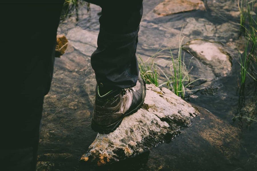 A hiking boot stepping onto a rock in a flowing stream